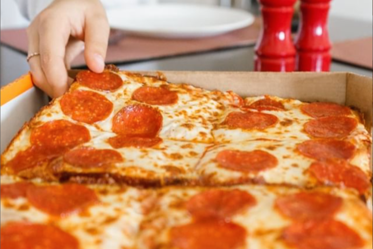 A hand picking up a slice of pepperoni pizza.