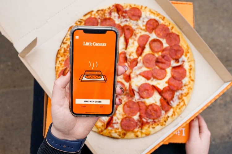 Person holding phone showing a pizza ordering app with a pepperoni pizza.